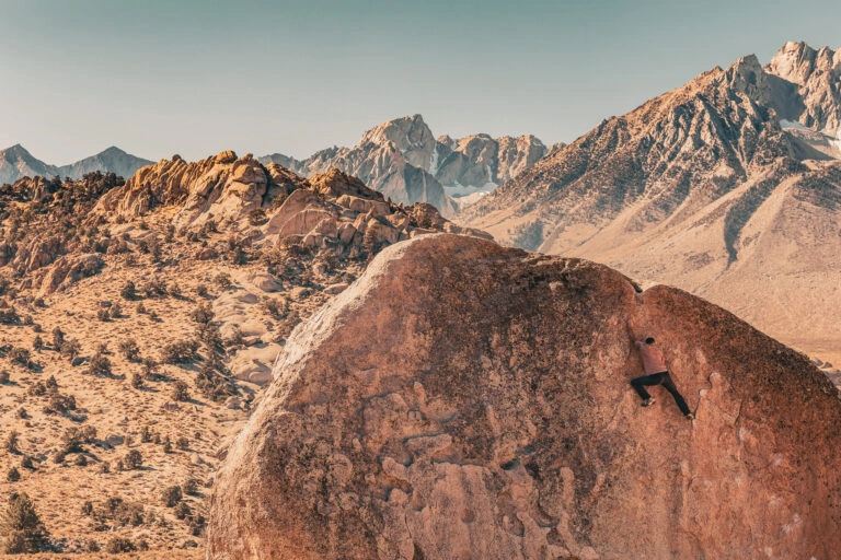 Man rock climbs on huge granite boulder in the Buttermilk area of Bishop, California with the Sierra Nevada behind
