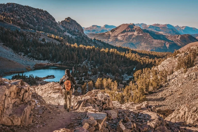 Day hiker descending the granite covered mountains in the John Muir Wilderness with Barney Lake and Mammoth Mountain in the background