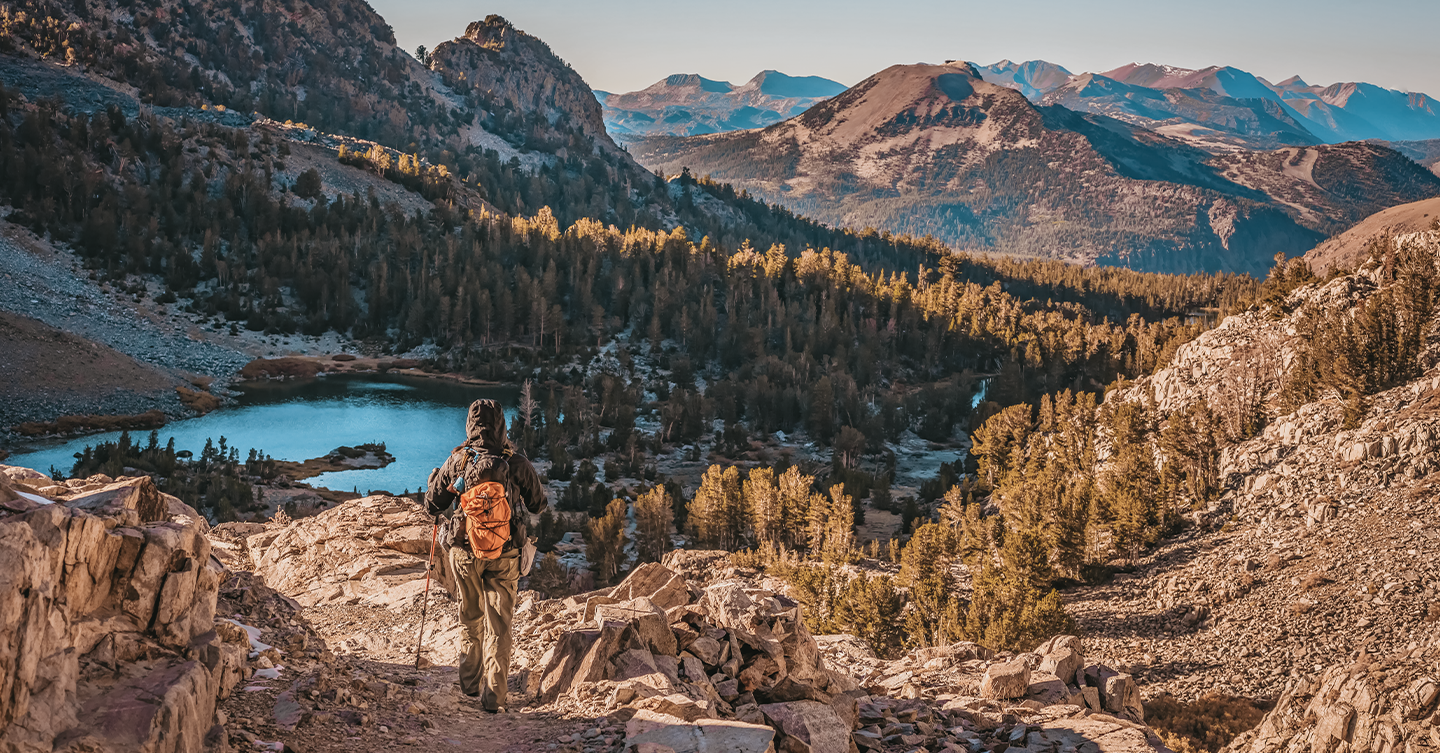 Day hiker descending the granite covered mountains in the John Muir Wilderness with Barney Lake and Mammoth Mountain in the background